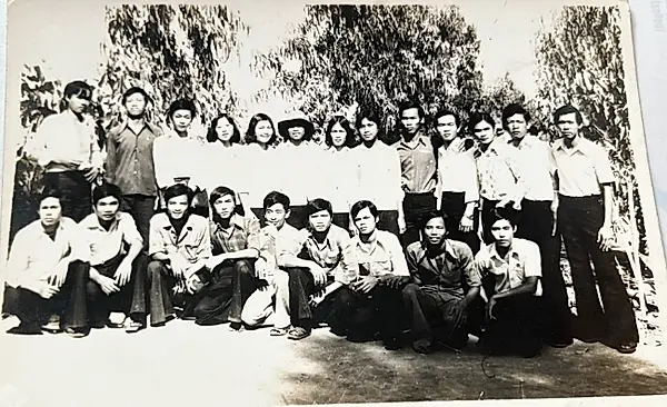 Ảnh đen trắng cũ: tập thể lớp 12B Khóa 2 chụp cùng thầy Thuận, hai hàng học sinh đứng và ngồi trước hàng cây